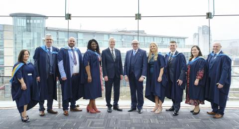 a group of people stand and pose for a photo with graduation gowns on