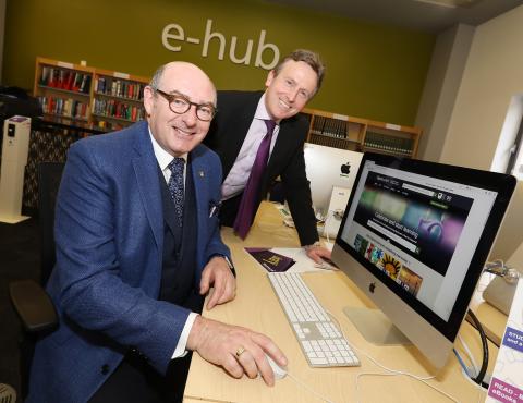 two men pose for a photo at a computer screen