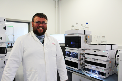 A man stands in a lab in a lab coat in front of some equiment