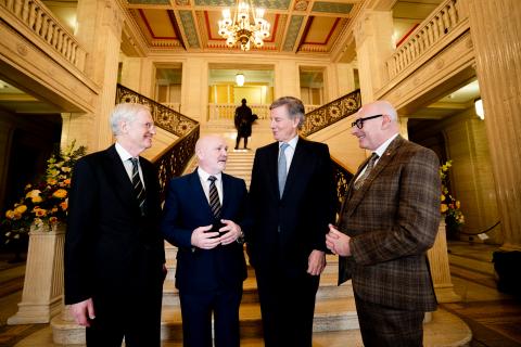 A group of men stand talking in an elegant room