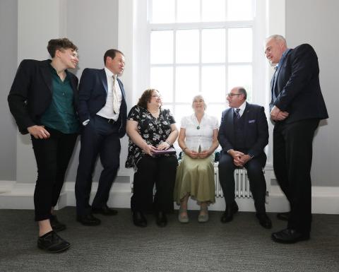 A group of people stand chatting around a window