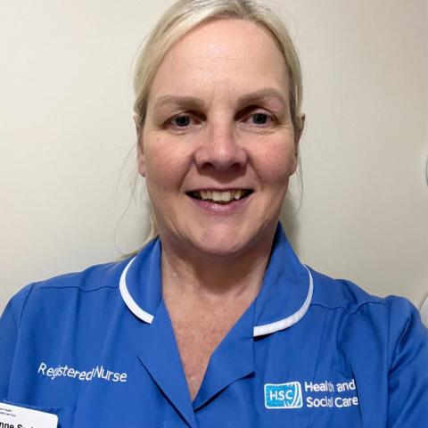 Anne Smith, wearing a blue Health and Social Care (HSC) uniform with a name badge reading “Anne Smith, Registered Nurse,” smiles at the camera against a plain light-coloured background.