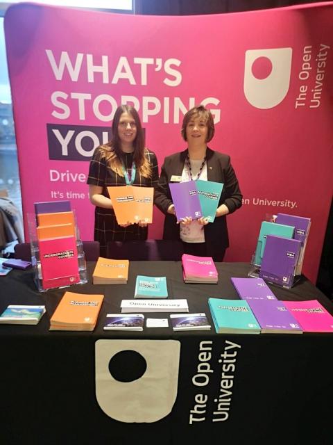 two woman stand at an Open University stand at an event