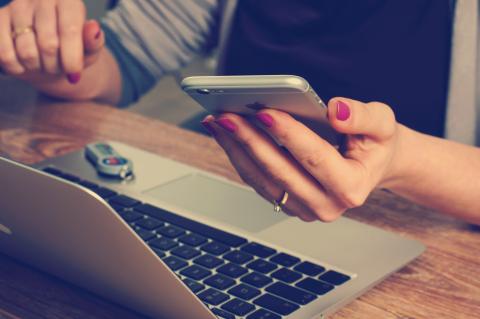 a woman looks at her phone whilst working on her laptop