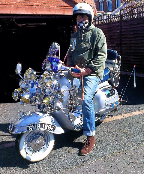 a man sits on a scooter wearing a helmet and green jacket and jeans