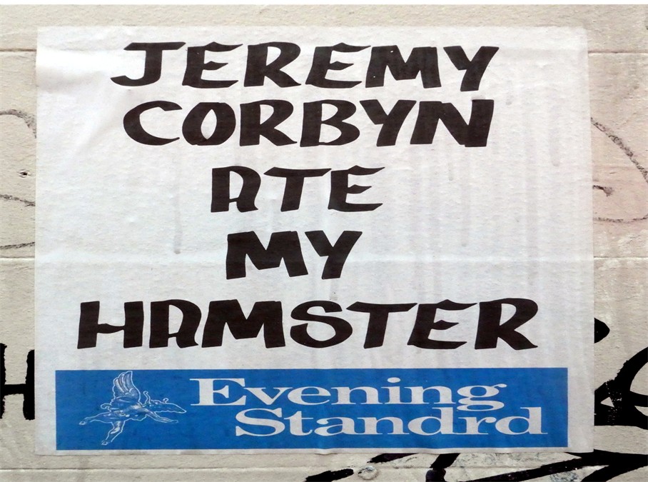 The image shows a paper sign, stuck onto a white wall. It has the wording 'Evening Stanard' at the bottom, with white writing on a blue background. Above it is the headline 'Jeremy Corbyn ate my hamster'. The headline is in black writing on a white background.