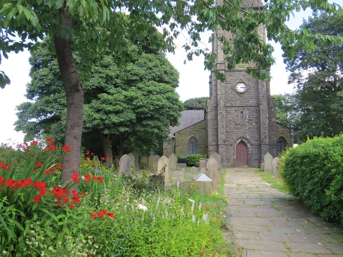 An image of a path leading to a churh. To either side is bushes, flowers and gravestones.