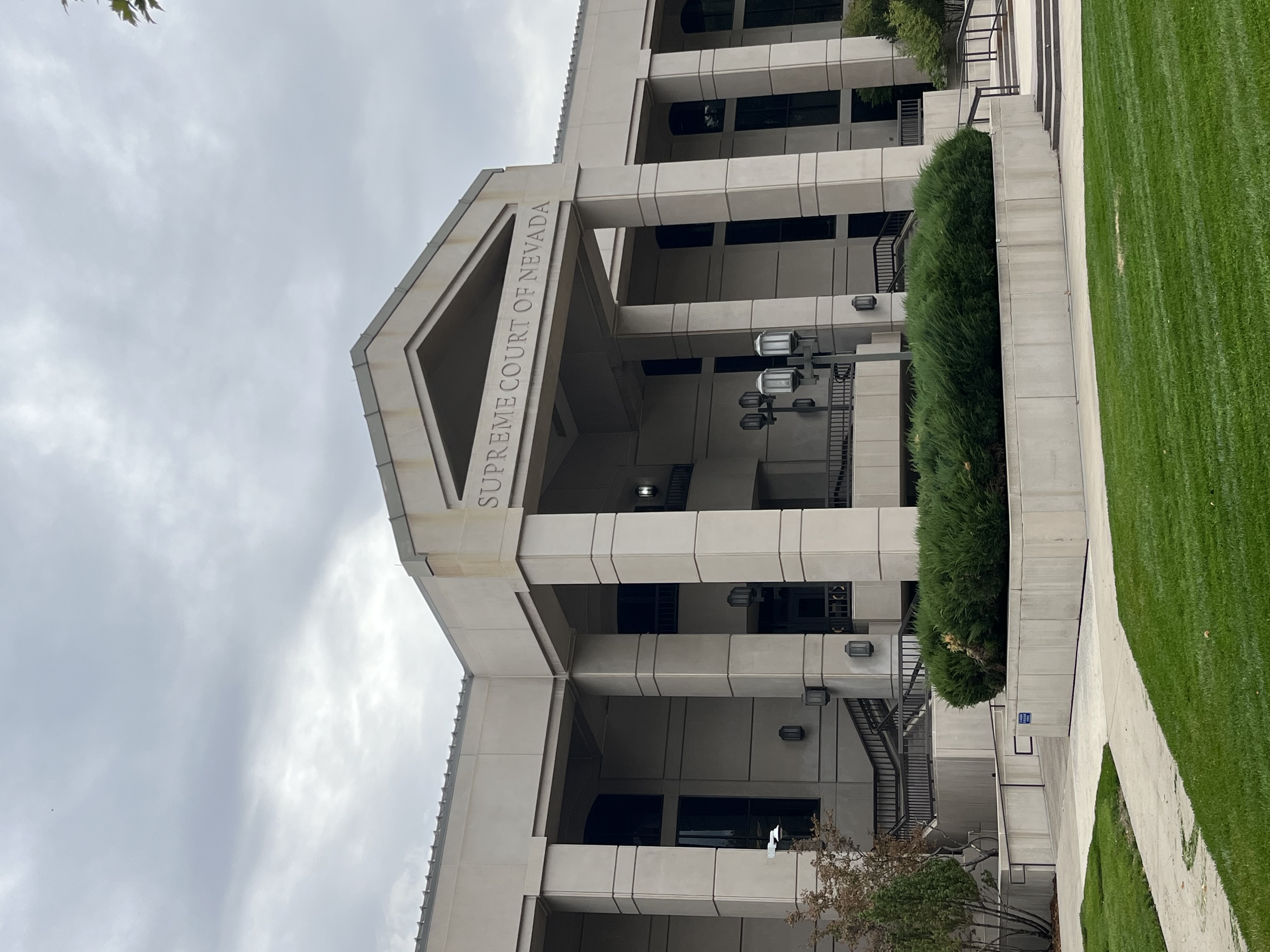 An image of a large building, with stairs leading up to it, and grass in front of it. Text along a beam towards the top of the building reads 'Supreme Court of Nevada'.