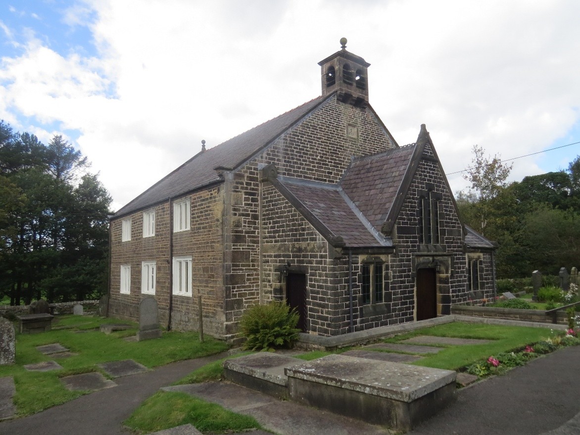 A stone chapel stands in the middle of the image, with grass and gravestones surrounding it.