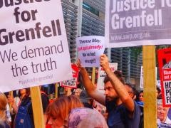 An image of a protest. The protest contains a number of placards and signs. One of the placards says 'Justice for Grenfell, we demand the truth.' A man is holding up a sign which says 'Theresa May just quit already. We've had enough!!!'