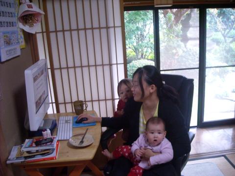 A woman sitting at a desk with two children working on a computer.