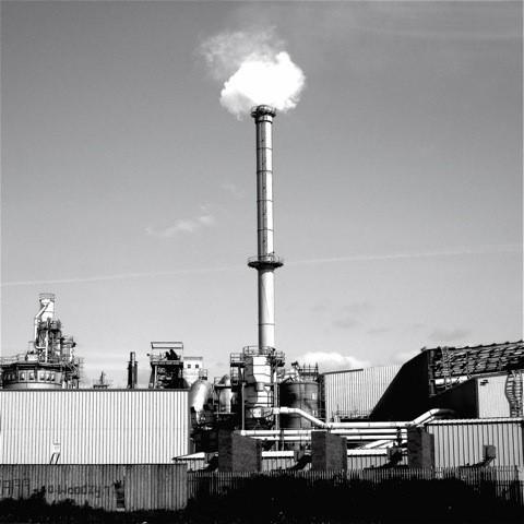 A facility showing a large chimney with smoke coming out of it.