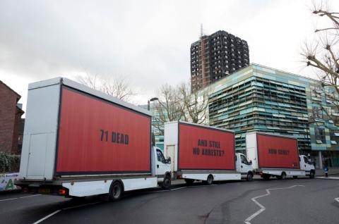 A set of three red billboards on vans outside Grenfell Tower that say '71 Dead', 'And Still No Arrests' and 'How Come?'