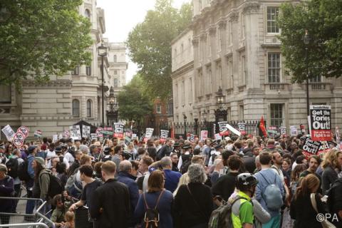 Protestors in the street with signs that say 'Get the tories out'.