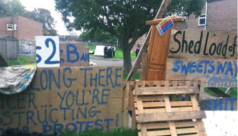 Residential area with wooden planks, a door, and other items, with protest signs.