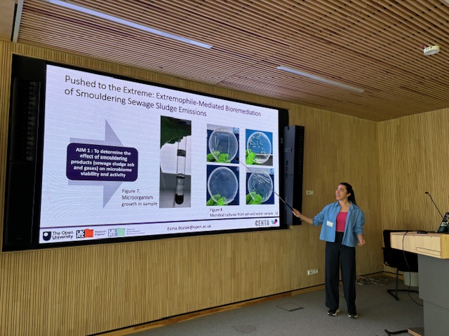 Esma presenting on a large screen with a pointer in a wooden panelled room