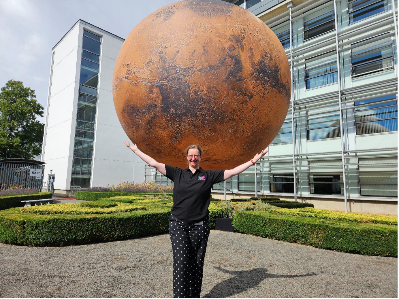 Prof Susanne Schwenzer stood in front of the large Mars globe, with her arm outstretched so it looks like she is holding up the installation