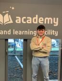 Olly stood wearing jeans, a beige fleece and a red lanyard.