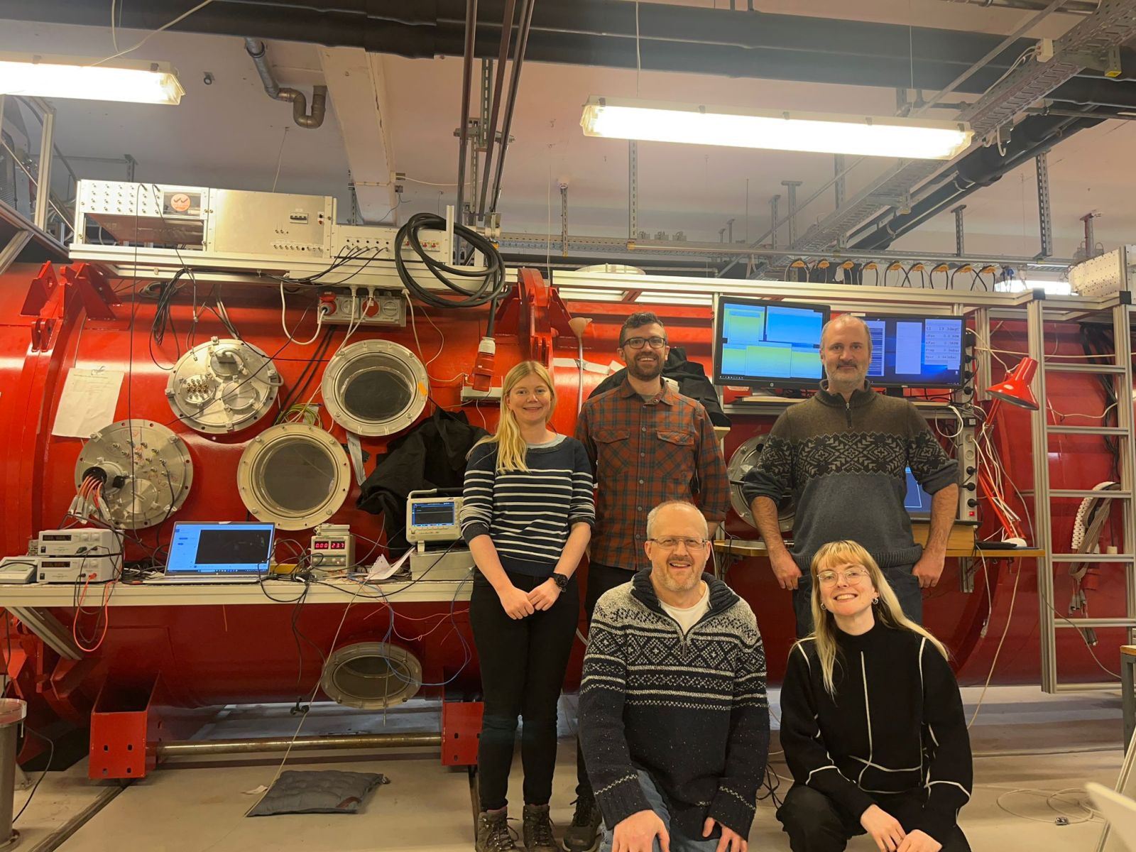 The Team posing in front of a piece of large red machinery 