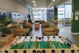a large open plan, bright area with sofas, a table football table, and potted plants.