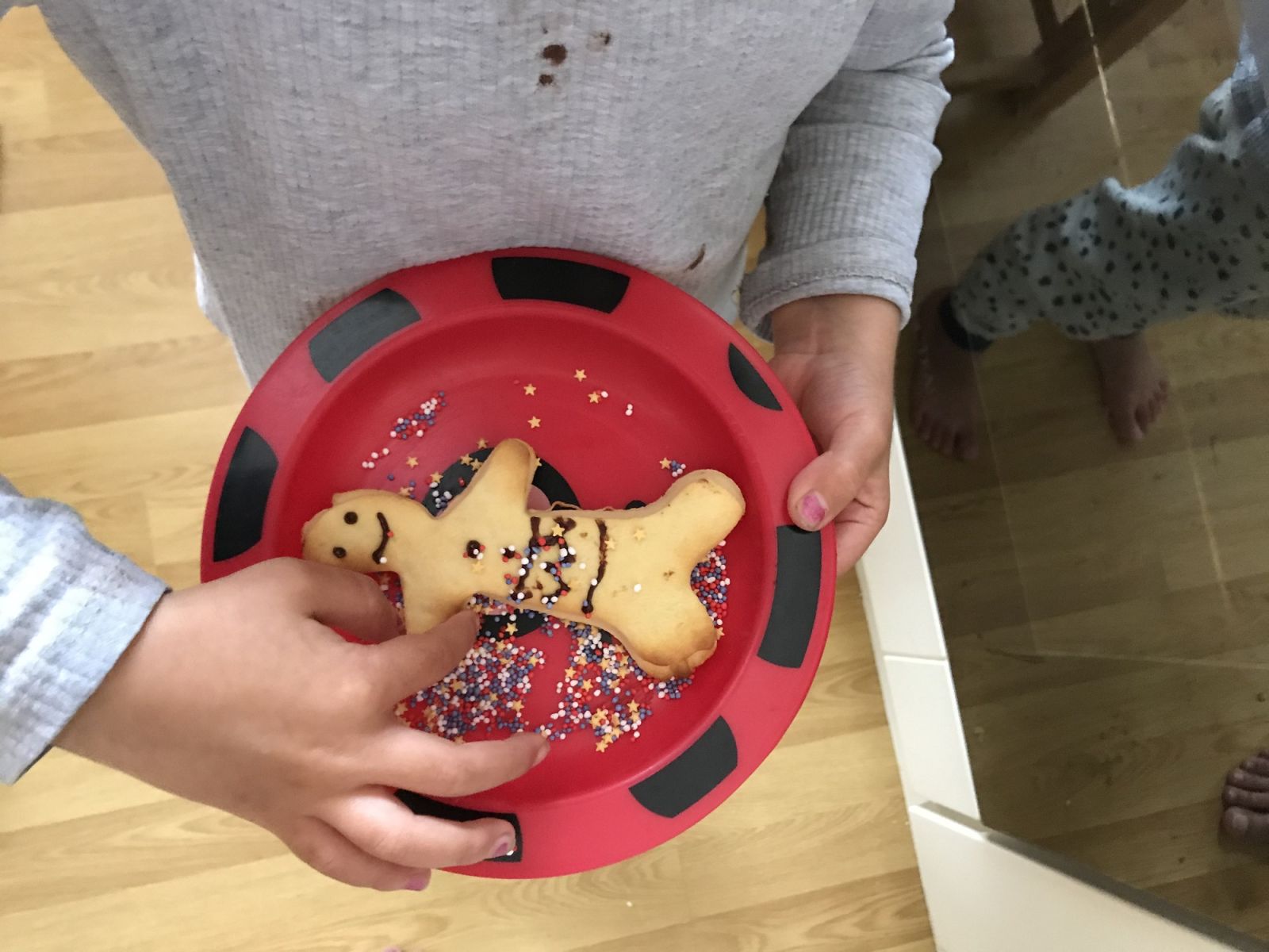 A small child holds a plate with a cookie shaped like a human on