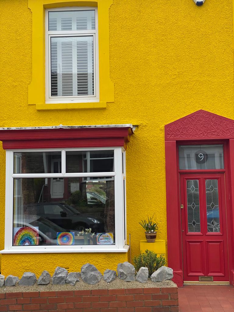 A colourful yellow house with a red door in South Wales supporting the NHS and care workers.