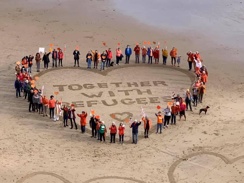 Refugees standing and forming a heart shape on the beach