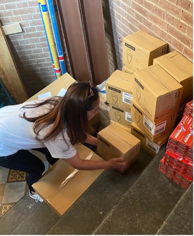 A woman wearing a white t-shirt is picking up boxes which are staked on the ground
