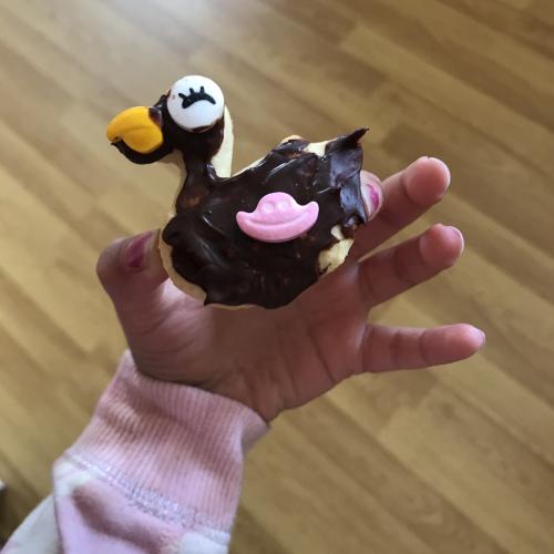 A duck-shaped biscuit is held by a small child. It has been decorated with a bright beak and white head