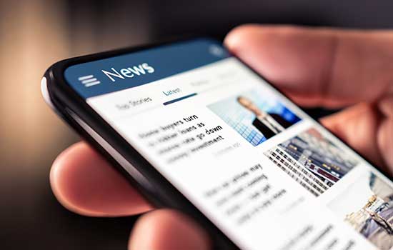 a close up of a hand holding a phone with news on the screen