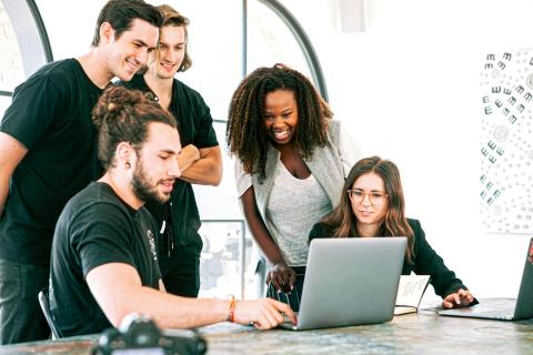 Team of people at a desk looking at a laptop screen.