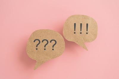 Two light brown speech bubbles on a salmon pink background, one containing question marks and the other containing exclamation marks