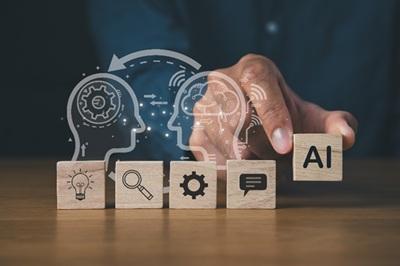 Hand placing an “AI” block among wooden icons representing ideas, search, settings, and chat, with abstract human head silhouettes in the background.