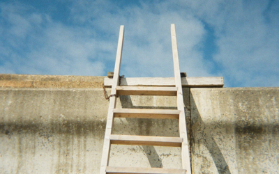A ladder leaning up against a concrete wall towards blue sky.