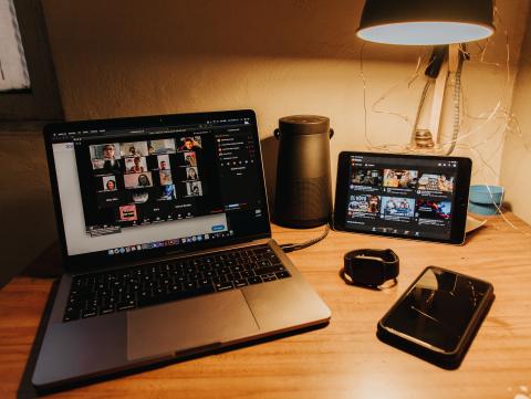 The photograph shows an online meeting taking place on the screen of a laptop and tablet