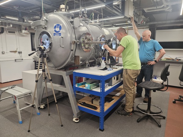 Image of Dr Petr Broz and Dr Matthew Sylvest positioning video cameras outside the George chamber before running an experiment