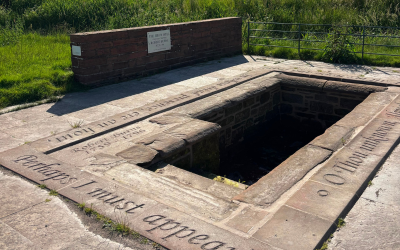 A well made of stone, surrounded by engraved slabs and brickwork, with inscriptions and a plaque dedicating the site to Robert Burns.
