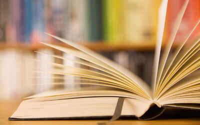 Photo of an open book in front of shelves full of books. 