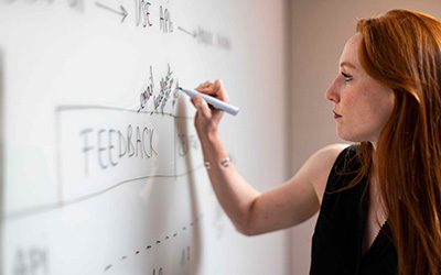 A woman standing, writing with a pen on a board