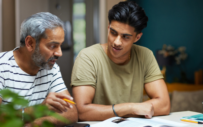 A father and son are reading over course material at the kitchen table