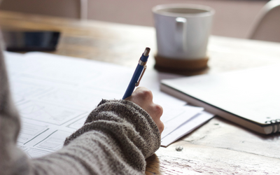 Photo of a hand writing in notebook in a cafe, by Green Chameleon on Unsplash