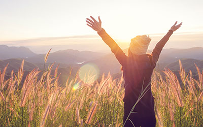 Woman in a meadow at sunrise, with arms outstretched