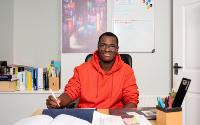 Student Joe, seated at a desk and holding a pen, with books and a tablet in front of him