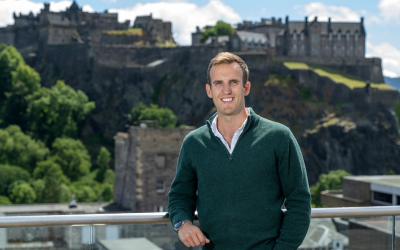 OU graduate Jonny Perriam leaning against railing in front of Edinburgh Castle