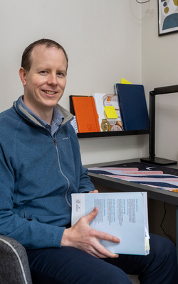 Stuart Borland, seated at a desk and holding a textbook. Photo by Neil Hanna.