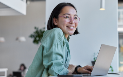 A woman with her laptop, smiling out the window