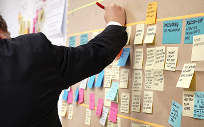 Post it notes on a wall, with an outstretched hand holding a pen