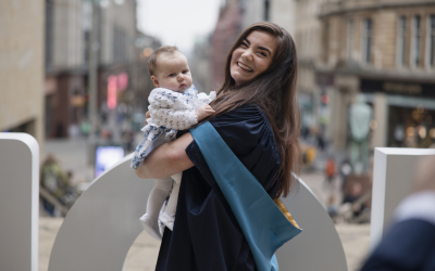 OU alumna Zara Mahon at her degree ceremony, with her child. Photo by Kathryn Tuckerman.