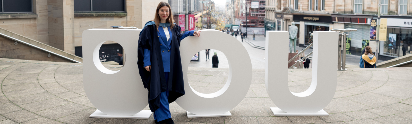 OU graduate standing in front of giant white letters.