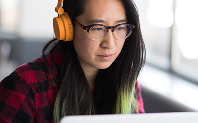 A woman with headphones on, looking at a laptop screen